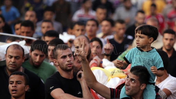 Man carrying his son gestures as mourners march during the funeral of three Palestinian boys from the Juda family and their mother, whom medics said were killed in an Israeli air strike, in Jabaliya in the northern Gaza Strip